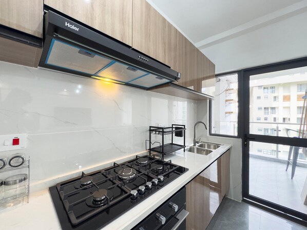 A modern kitchen with a gas stove, a black range hood, and a window with a view of a building.
