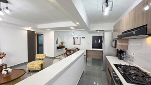 A modern kitchen with a gas stove, a microwave, and a refrigerator. There is a dining area with a table and chairs. - Winchester Garden (Nairobi)