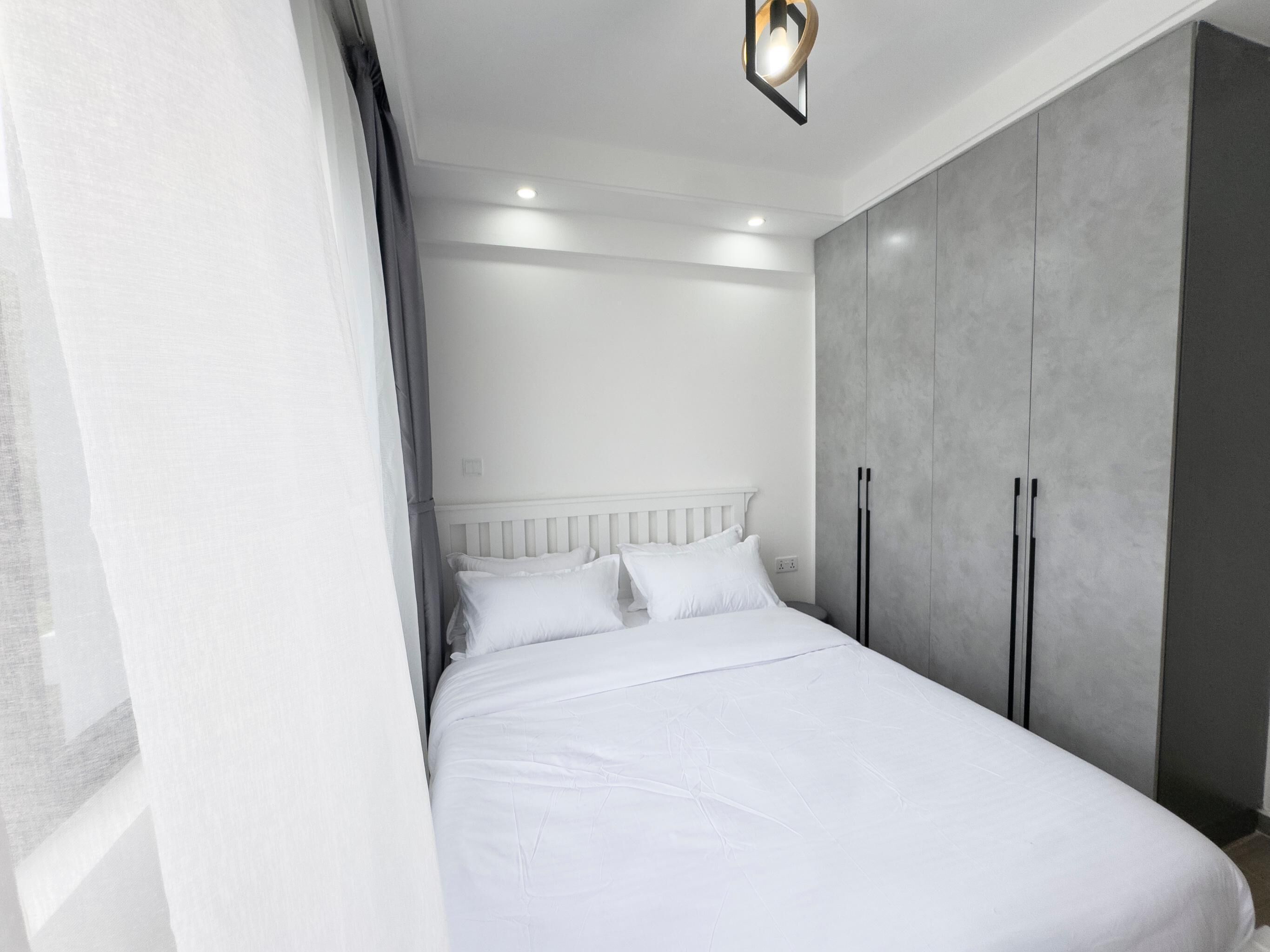 Ein modernes Schlafzimmer mit einem weißen Bett, einem grauen Kleiderschrank und einer Deckenleuchte.