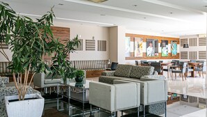A modern hotel lobby with a sofa, chairs, a coffee table, and a large potted plant. - Gastronomy | Gym | Pool #ITA10 (Florianópolis)