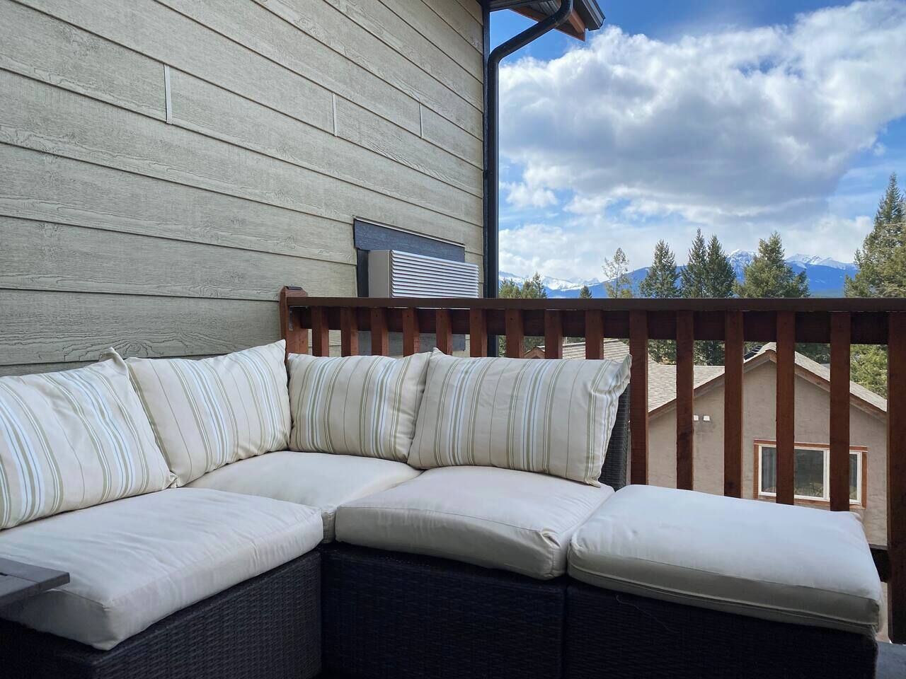 A sectional sofa with striped cushions on an outdoor deck with a wooden railing.
