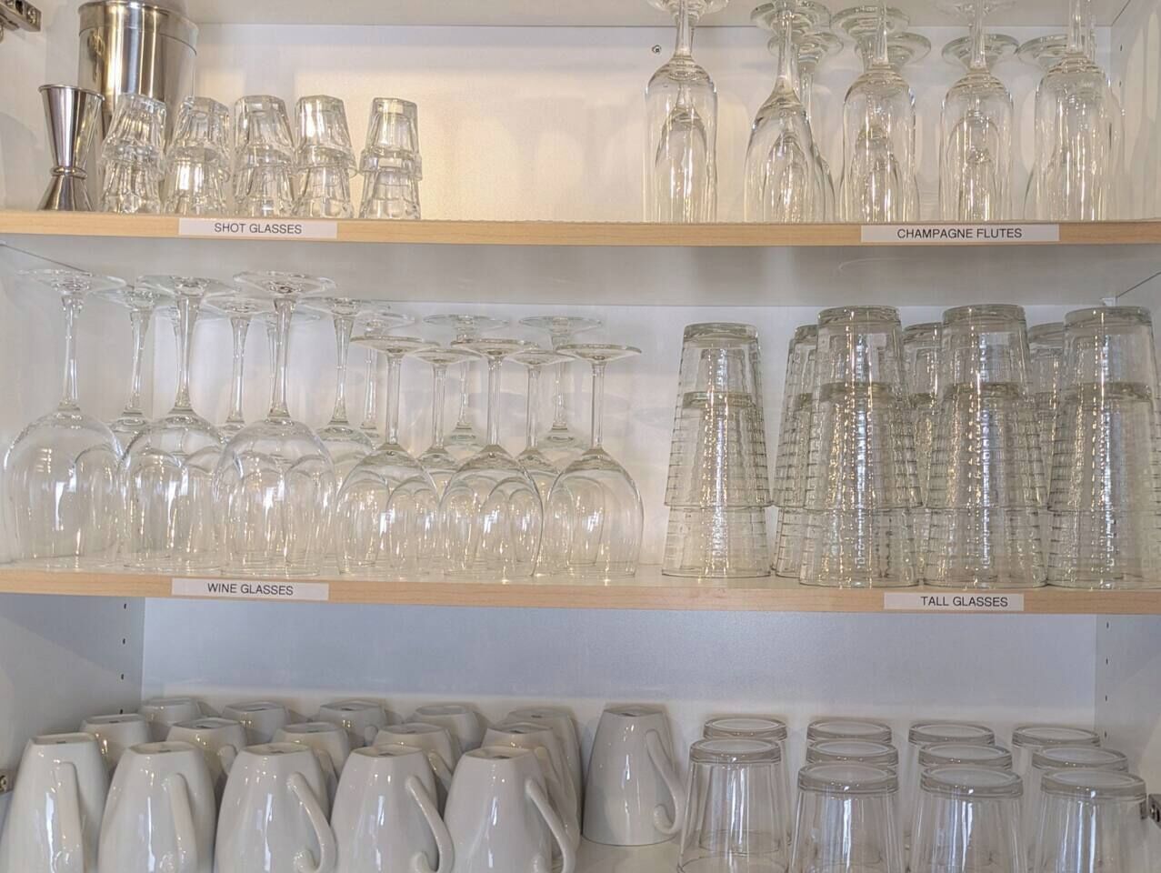 Shelves with various types of glasses including shot glasses, champagne flutes, wine glasses, and tall glasses.