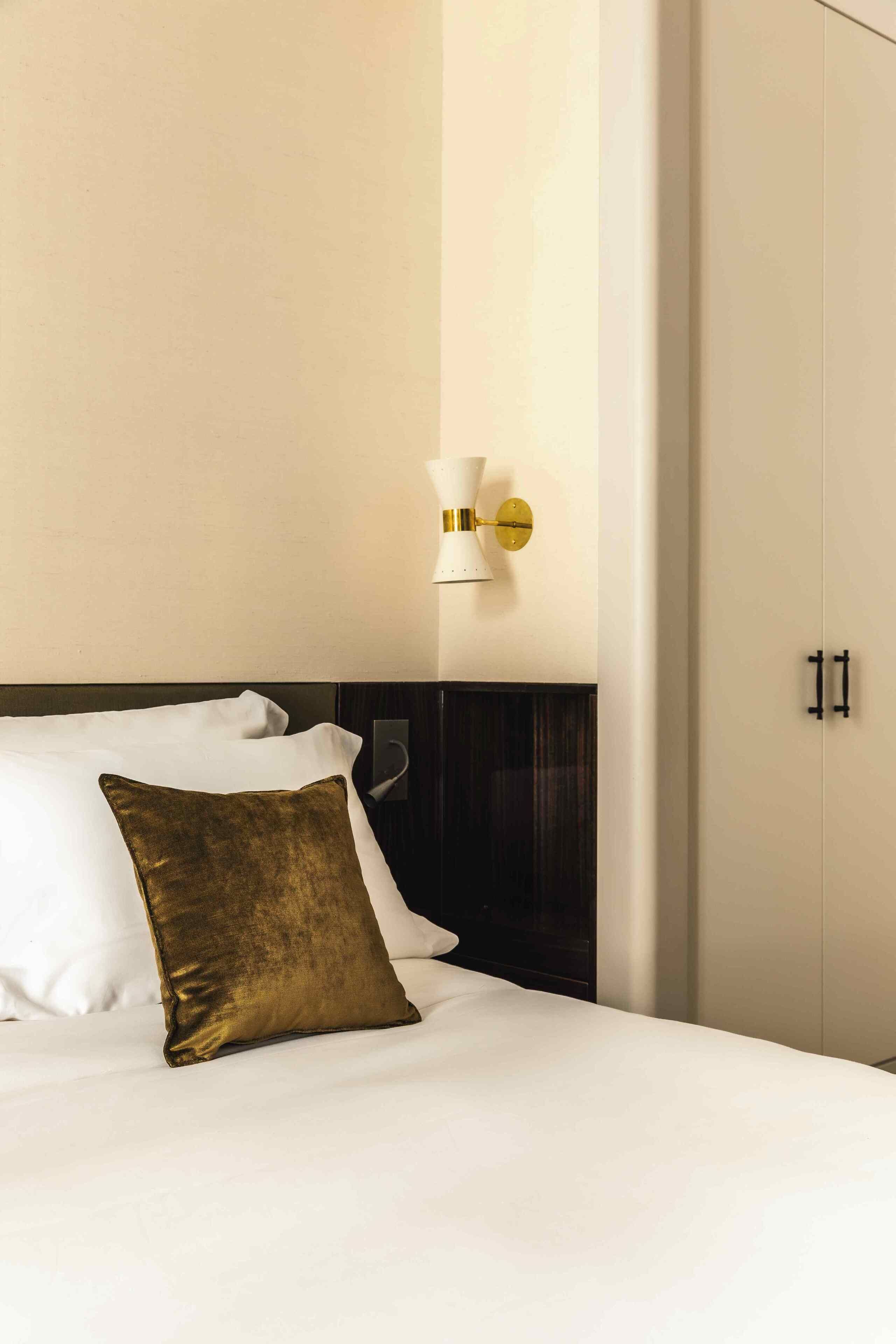 A hotel room with a bed, a nightstand, a wall-mounted lamp, and a wardrobe.