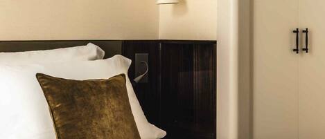 A hotel room with a bed, a nightstand, a wall-mounted lamp, and a wardrobe.