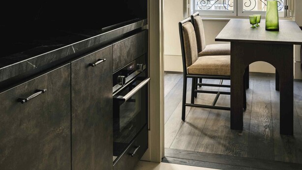 A modern kitchen with dark cabinetry, a built-in oven, and a dining area with a table and chairs. - Mondovi Luxury Suites (Paris)