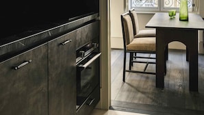 Une cuisine moderne avec des meubles de couleur sombre, un four encastré et un coin repas comprenant une table et des chaises.