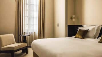 A hotel room with a large bed, a chair, a small table, and a nightstand.