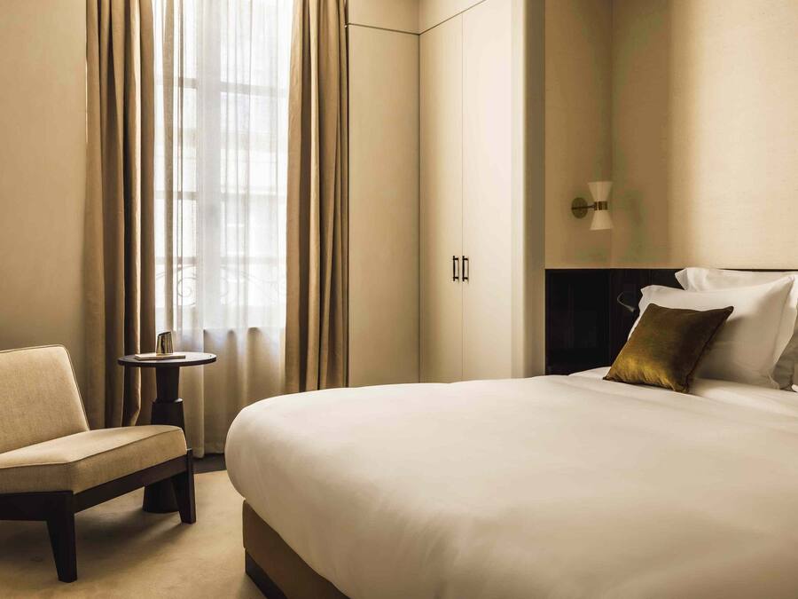 A hotel room with a large bed, a chair, a small table, and a nightstand.