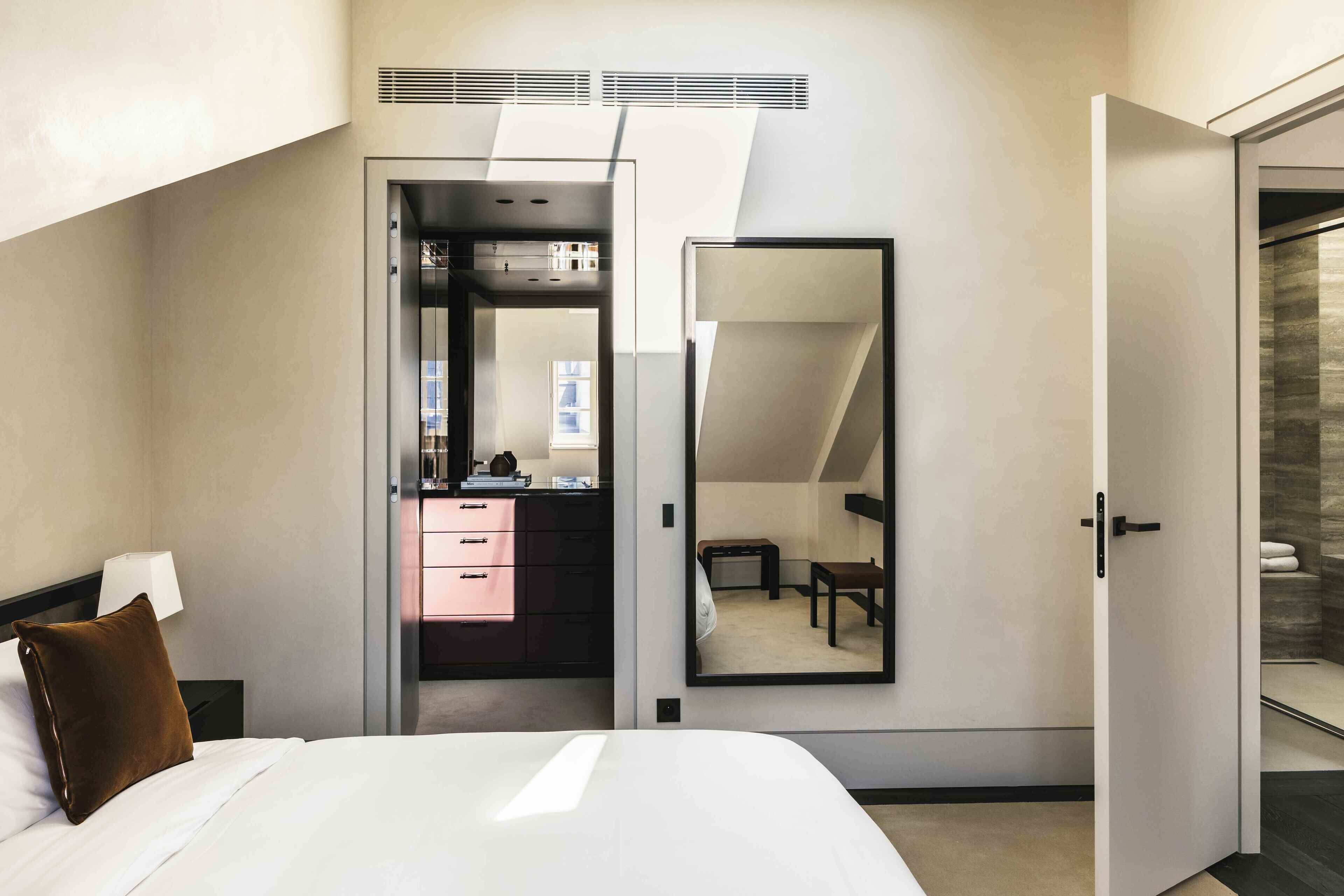 Une chambre d’hôtel moderne dotée d’un grand lit, d’un dressing, d’un miroir et d’un espace douche.