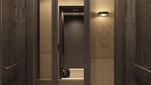 Un ascenseur moderne au design minimaliste, doté d’un mur texturé et d’un luminaire placé sur le côté.