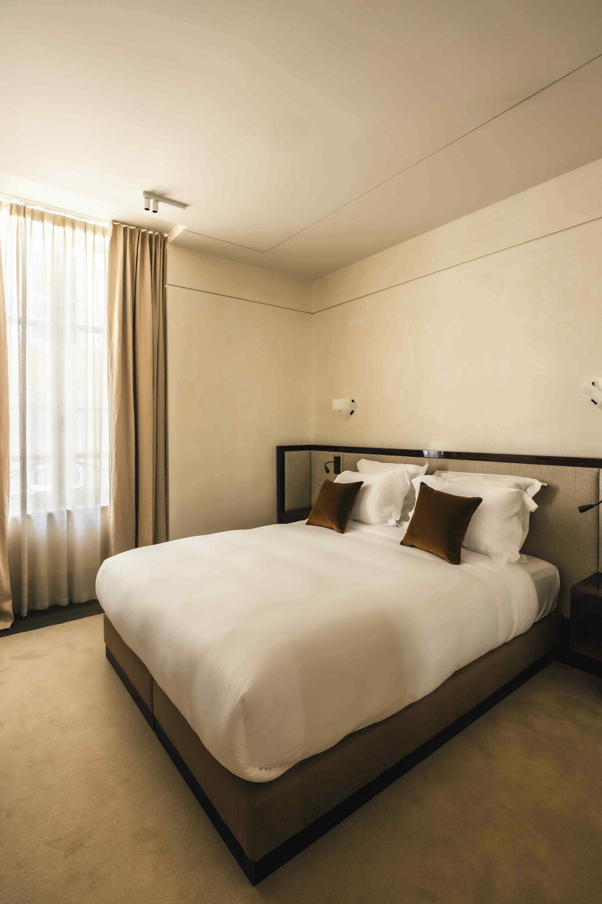A hotel room with a large bed, a nightstand, a ceiling light, and a window with curtains.