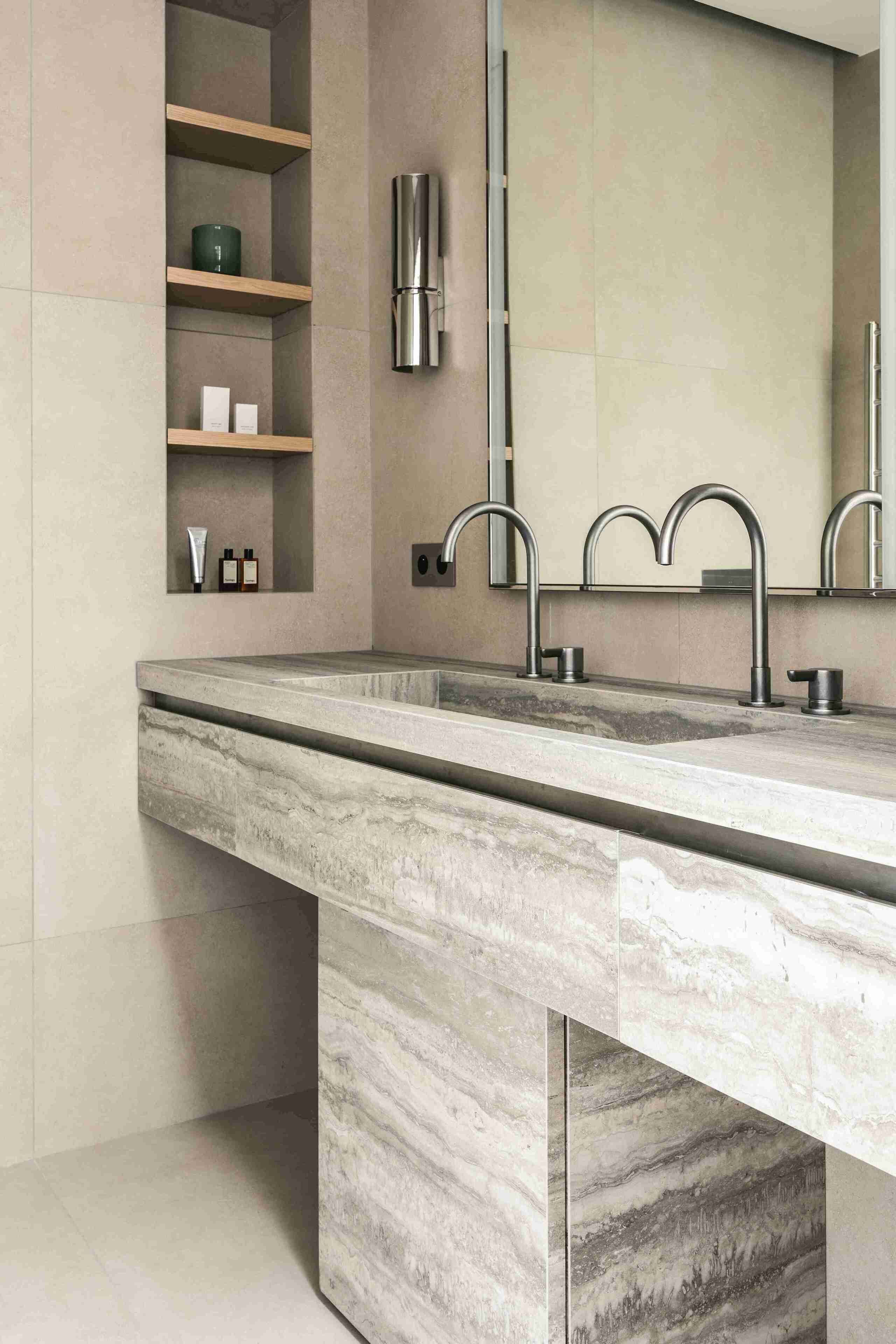 A modern bathroom with a marble sink, built-in shelves, and a large mirror.