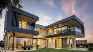 Una casa moderna de dos pisos con amplios ventanales de vidrio, techo plano y césped cuidado.