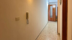 En hall med en telefon, en väggmonterad lampa och en trädörr längst in.
