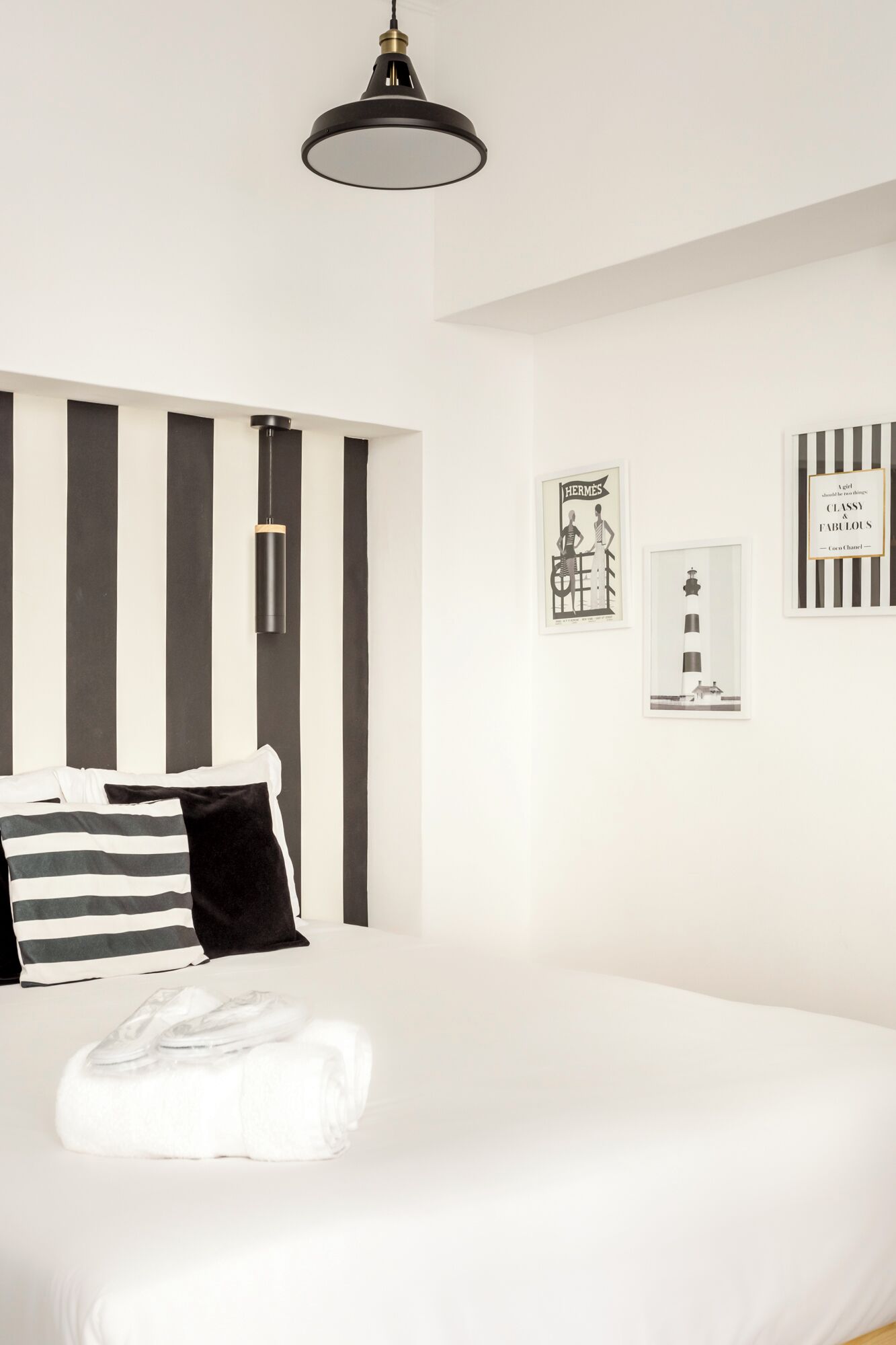 A modern bedroom with a large bed, black and white striped headboard, and a pendant light.