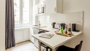 Une cuisine moderne avec des meubles blancs, un plan de travail en marbre et une fenêtre agrémentée de rideaux.