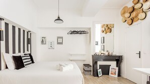 Une chambre avec un grand lit, un luminaire suspendu, une cheminée noire et un miroir orné de chapeaux.