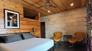 A bedroom with a bed, two chairs, a ceiling fan, and a wooden ceiling. - CHRISTOVAL CASITAS #5 KING ROOM (Christoval)