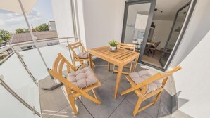 A balcony with a wooden table and chairs, a potted plant, and a view of the building's interior.
