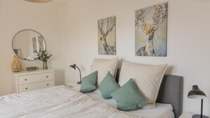 A bedroom with a bed, pillows, a bedside table, a lamp, a dresser, a mirror, and two wall paintings.