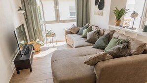 A living room with a beige sofa, a television on a stand, a small side table, and a potted plant.