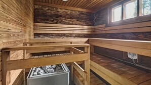 A wooden cabin interior with a sloped ceiling, a window, and a fireplace with a storage bin below. - Bliss Adventure Lodge (Pelkosenniemi)