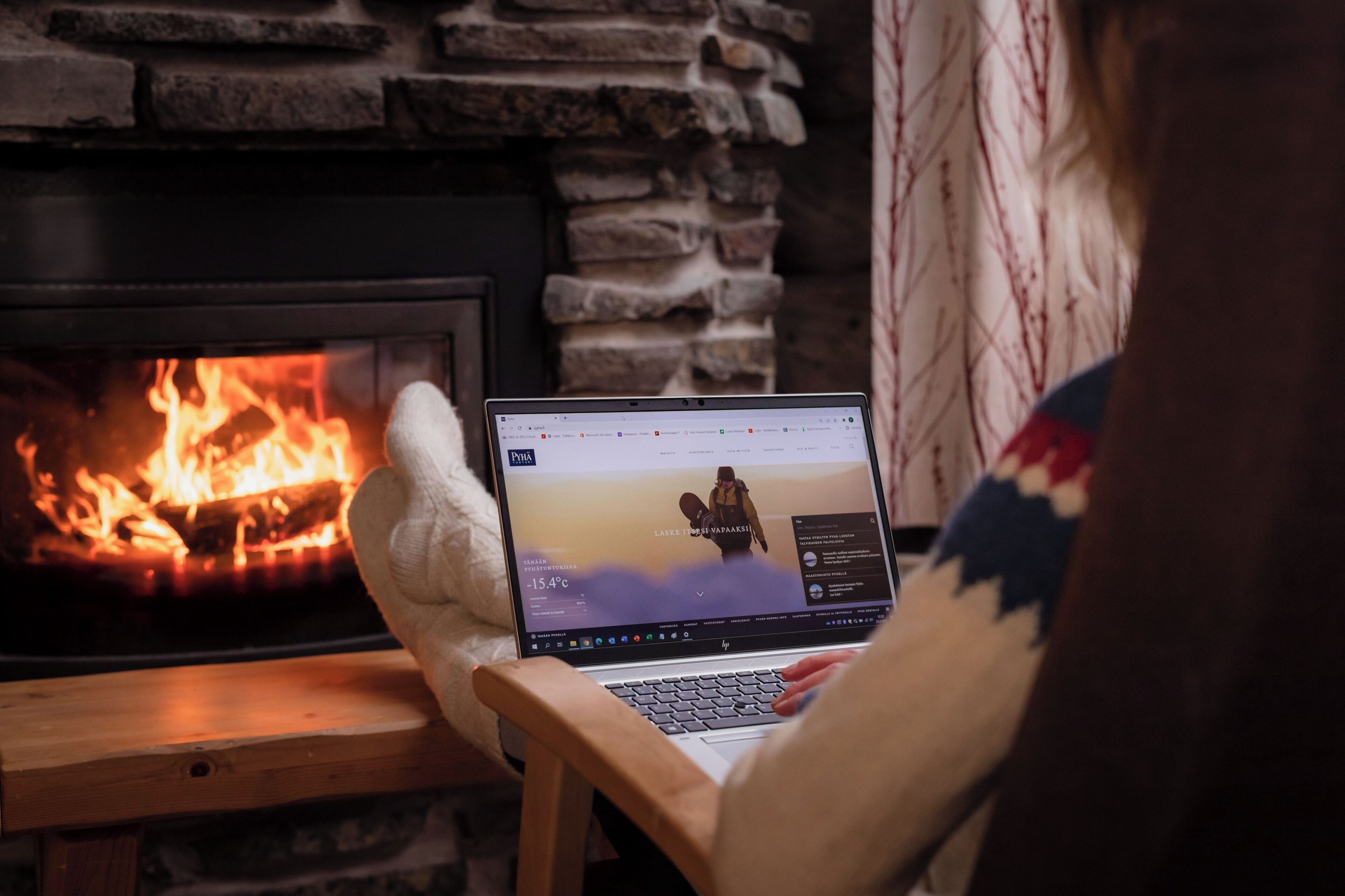 A laptop on a wooden chair in front of a fireplace with visible flames.