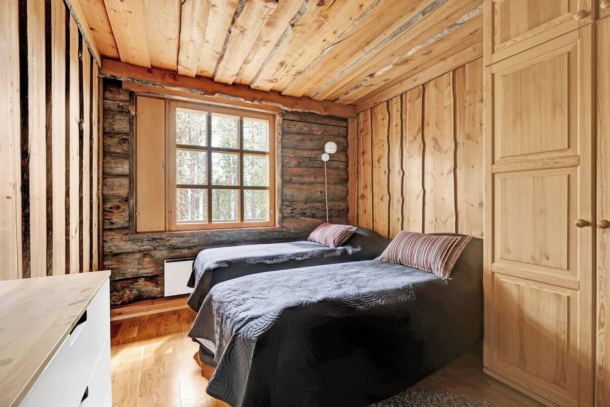 Una habitación tipo cabaña con dos camas, techo de madera, un ventanal grande y un armario.