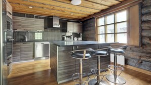 A modern kitchen with a wooden ceiling, stainless steel appliances, and a large island with bar stools. - Bliss Adventure Lodge (Pelkosenniemi)