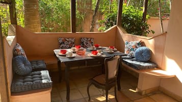 Relax in a serene outdoor space with a beautifully set table for tea, surrounded by lush greenery and comfortable seating.