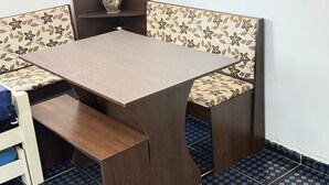 A corner dining table with floral-patterned cushioned benches, a small potted orchid, and a wooden shelf above. - Feet in the Sand Tupi Beach (Praia Grande)
