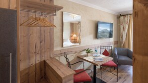 A hotel room with wooden paneling, a dining area with a table and chairs, a TV mounted on the wall, and a window with curtains. - The Rotspitz / Achensee (Tirol)