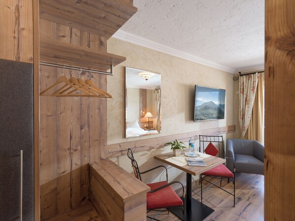 A hotel room with wooden paneling, a dining area with a table and chairs, a TV mounted on the wall, and a window with curtains. - The Rotspitz / Achensee (Tirol)