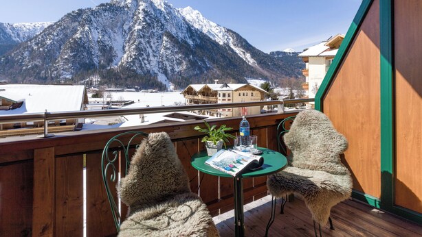 A balcony with a view of snow-covered mountains, wooden furniture, and a table with a bottle and glasses. - The Rotspitz / Achensee (Tirol)