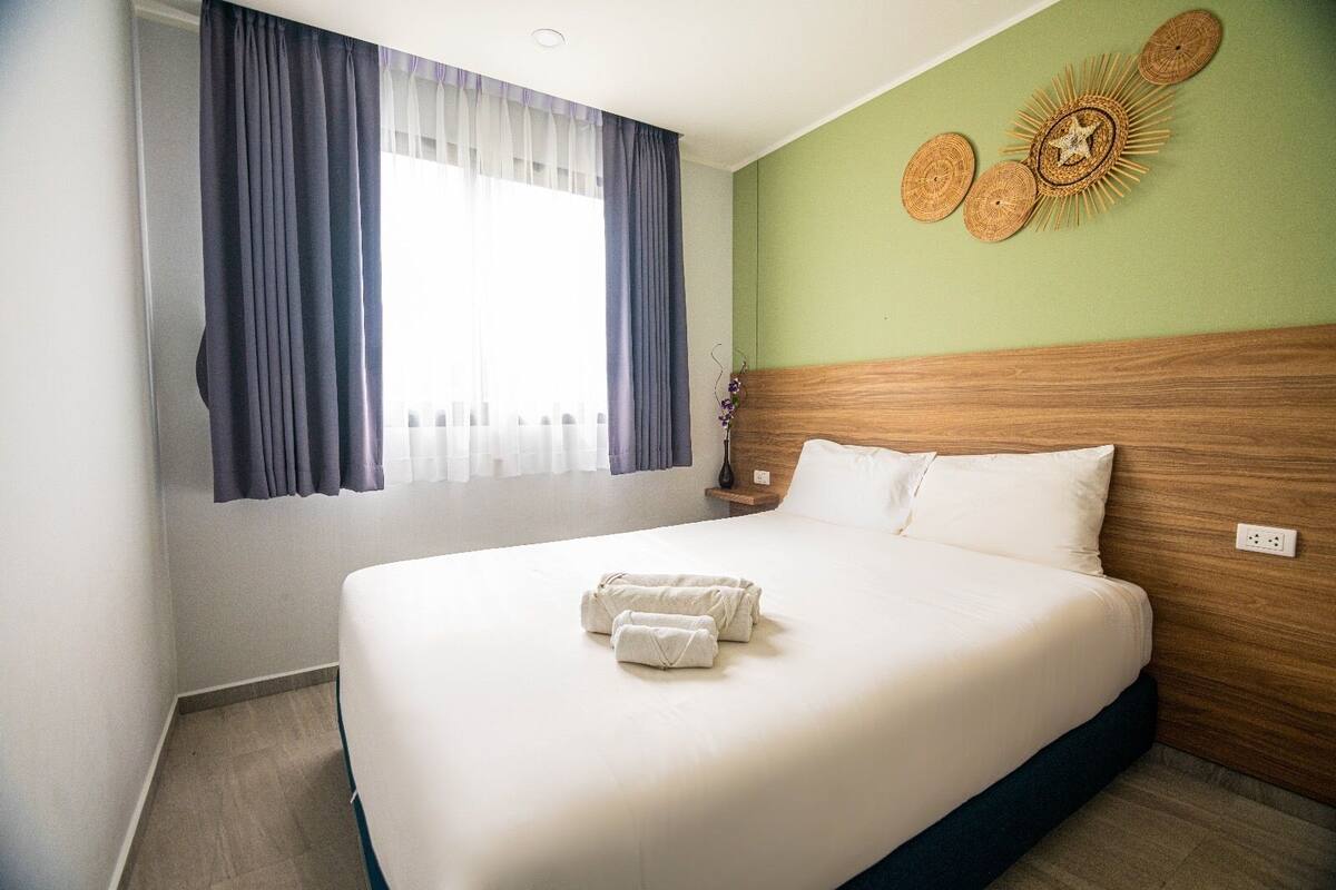 A hotel room with a large bed, a wooden headboard, a green accent wall, and a window with curtains.