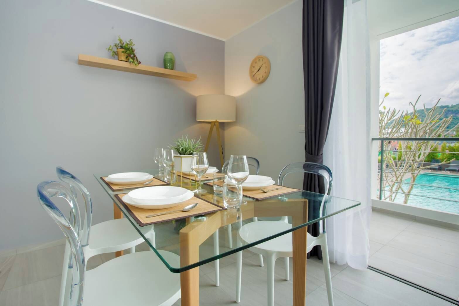 Un comedor con mesa de vidrio, sillas blancas y vistas a una piscina.