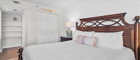 A bedroom with a wooden headboard, a bed with white bedding, a nightstand with a lamp, and a white wardrobe with louvered doors.