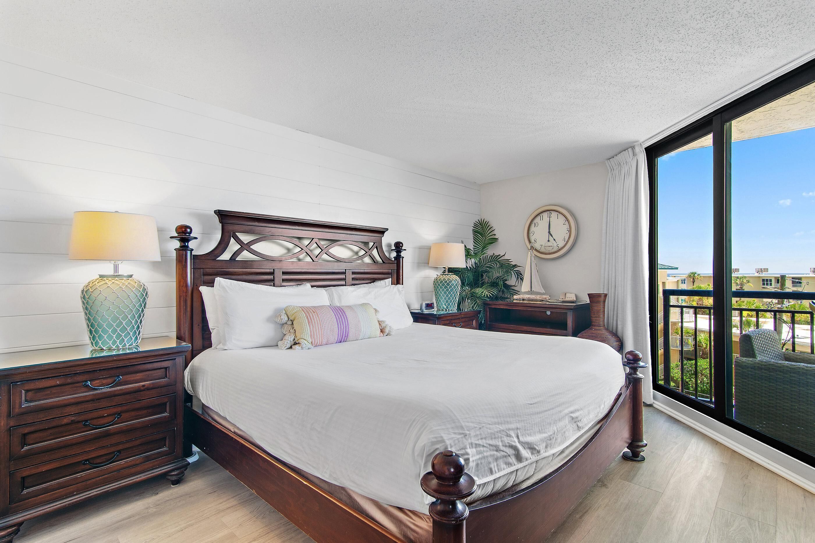 Une chambre d’hôtel avec un grand lit, deux tables de chevet, une horloge et une fenêtre donnant sur un beau paysage.