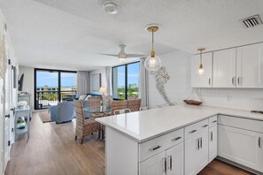 A modern kitchen with white cabinets, a central island, and a dining area with wicker furniture. - Sundestin 518 (Destin)