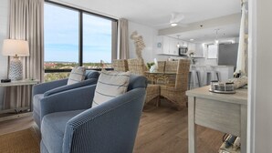 A modern living room with a sofa, a dining area with wicker furniture, and a kitchen with white cabinets. - Sundestin 518 (Destin)