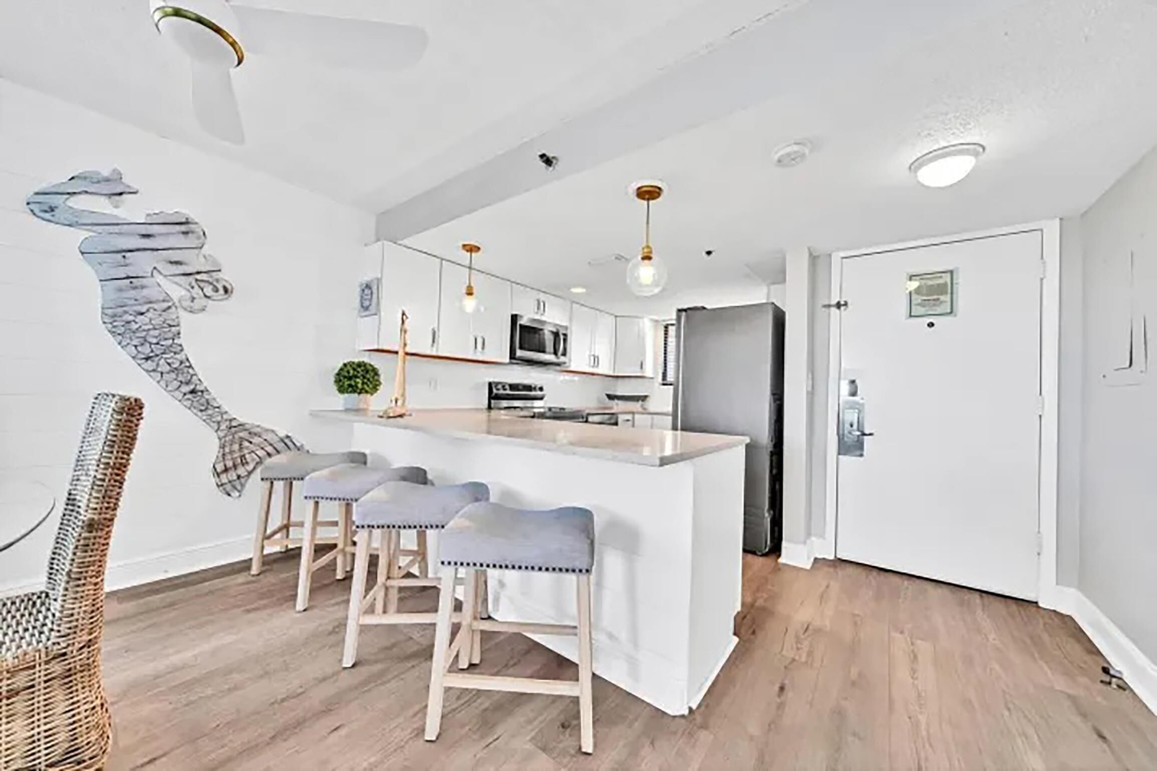 A modern kitchen with white cabinetry, a central island with bar stools, and a dining area with wicker chairs.