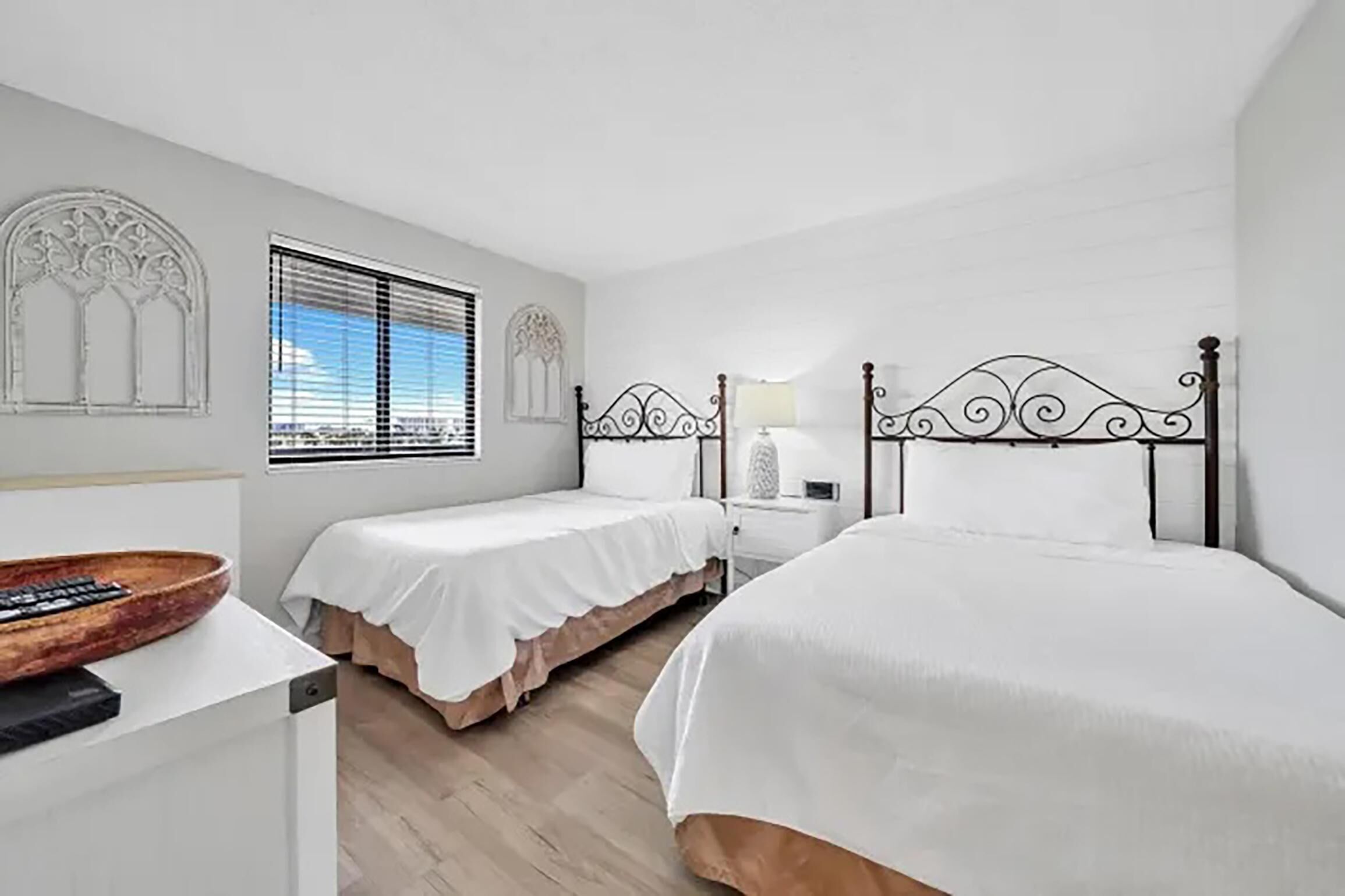 Un dormitorio con dos camas, una mesita de noche de madera y una ventana con persianas.