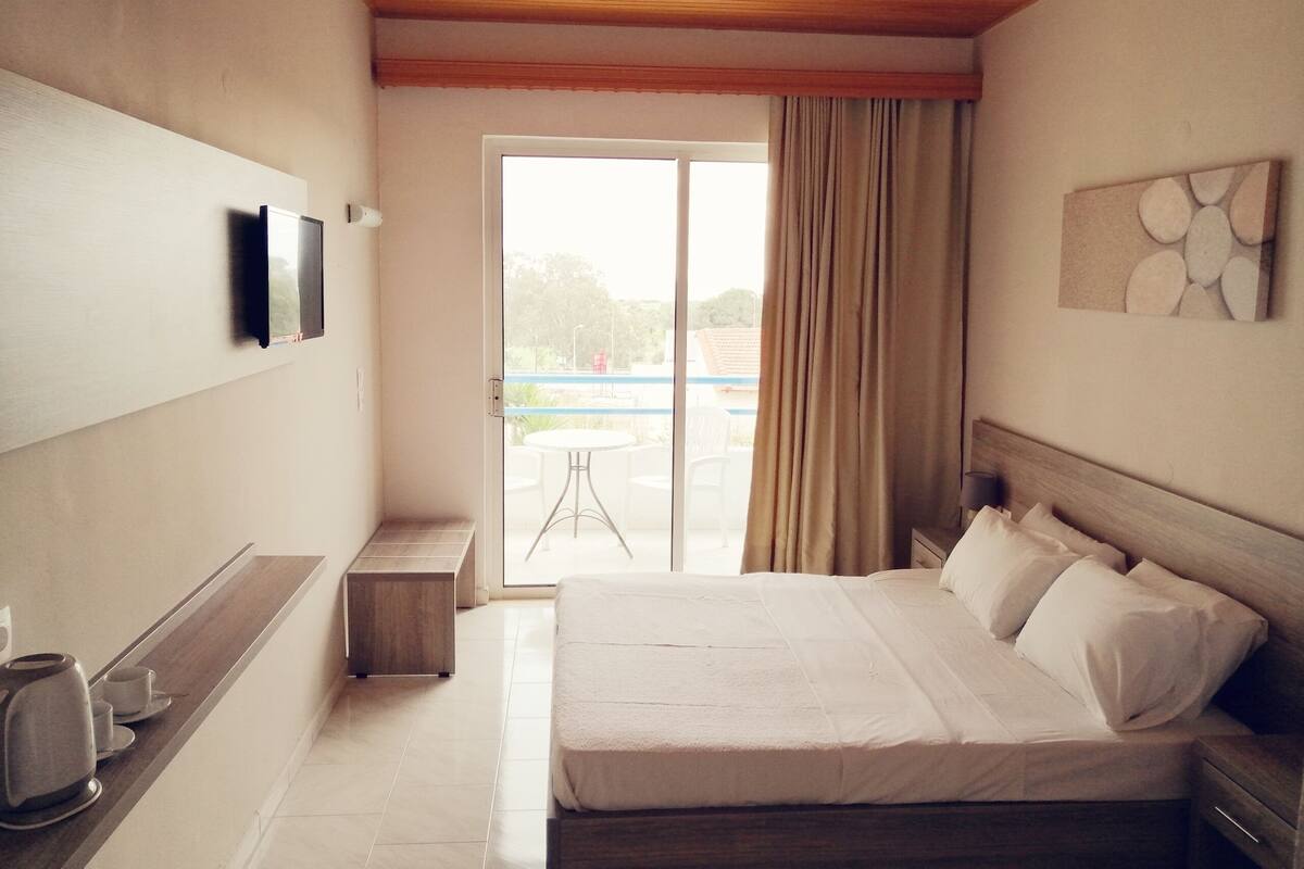 Habitación de hotel con cama, mesita de noche y televisor montado en la pared.