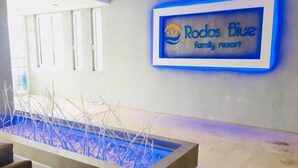A reception area with a sign for Rodos Blue family resort, a concrete planter with branches, and a modern interior design. - Celadi vista (Rhodes)