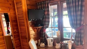 A wooden cabin interior with a wooden desk, a chair, a television mounted on the wall, and a window with plaid curtains. - Family Cabin Ben Morecrianlarich, West Highland (Crianlarich)