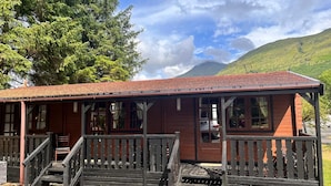 A wooden cabin with a porch and steps, surrounded by trees and a mountain in the background. - Family Cabin Ben Morecrianlarich, West Highland (Crianlarich)