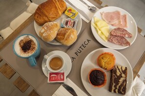 Aamiaispöytä, jossa on croissantteja, leivonnaisia, juustoa, kinkkua ja muffinssi.