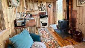 A cozy cabin interior with a wooden ceiling, a kitchenette, a fireplace, and a blue sofa.