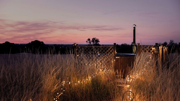 A wooden deck with a barbecue grill, surrounded by tall grass and string lights.