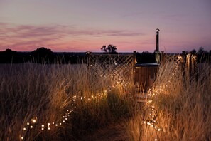 A wooden deck with a barbecue grill, surrounded by tall grass and string lights.